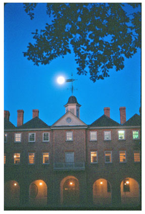The Wren Building at night with lights in the second floor windows and first floor arches.