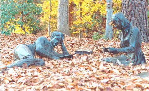 Statue of two students, one sitting and one reclining on the ground reading a book