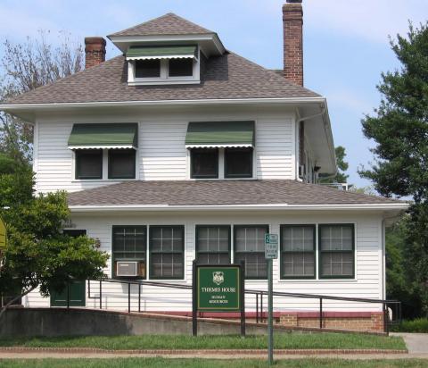 Two story white house with window awnings and an accessible ramp entrance in the front