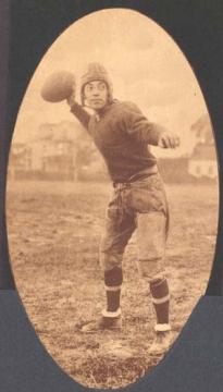 Black and white photo of Matsu in padded football gear and holding a football in the air