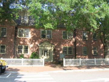 Two story brick building with a white picket fence and trees in front