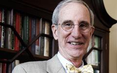 Geoffrey Feiss standing in front of a bookcase and wearing a gray suit and yellow bow tie