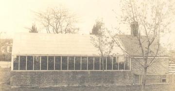 Black and white photo of the single story greenhouse with brick foundation and glass sides and roof