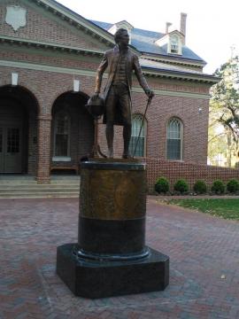 Bronze statue of James Monroe standing in a waist coat and carrying a cane on top of a plinth