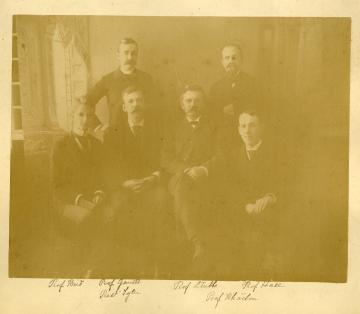 Yellowed, historic photograph of the Six Wise Men, four seated and two standing wearing dark suits