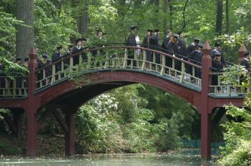 Graduating students walk over the Crim Dell pond on a red painted arched bridge
